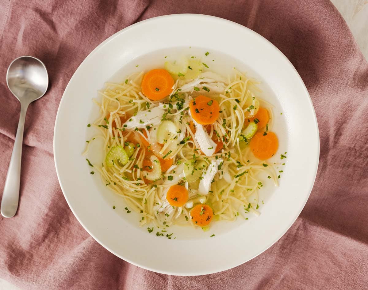 Bowl of clear chicken broth with noodles, pieces of chicken, and sliced carrots