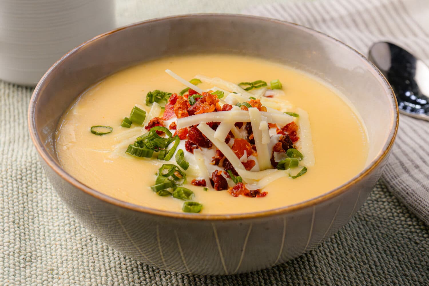 Bowl of potato soup with green onion, diced bacon, and melted cheese